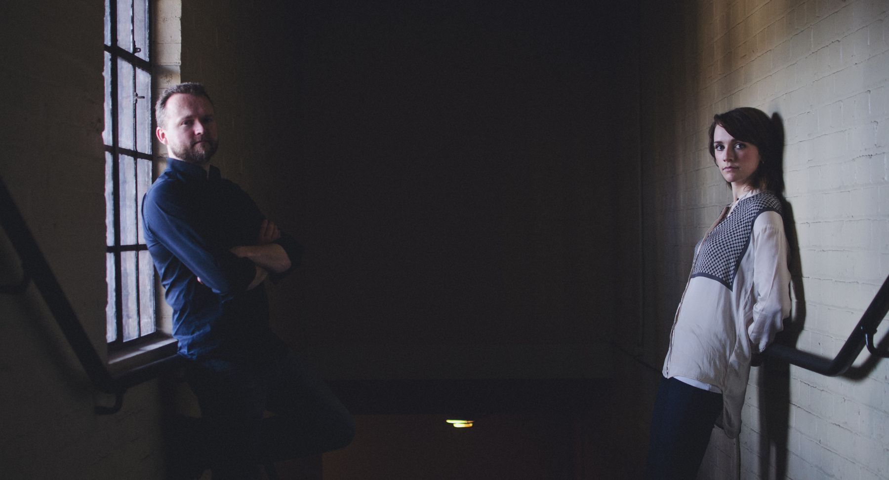 Luke and Charlotte Ritchie on a stairwell, lit by a tall window